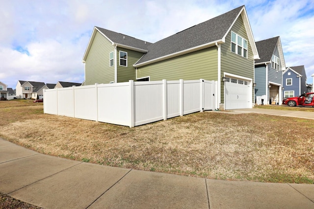 view of side of property with driveway, an attached garage, fence, and a residential view