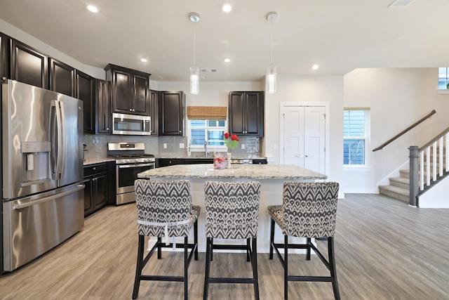 kitchen with pendant lighting, stainless steel appliances, a kitchen island, light stone countertops, and light wood-type flooring