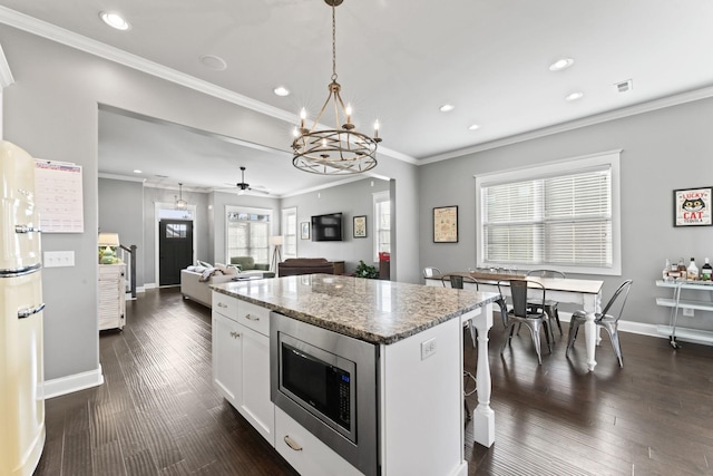 kitchen featuring a breakfast bar area, stone countertops, stainless steel microwave, a kitchen island, and white cabinets