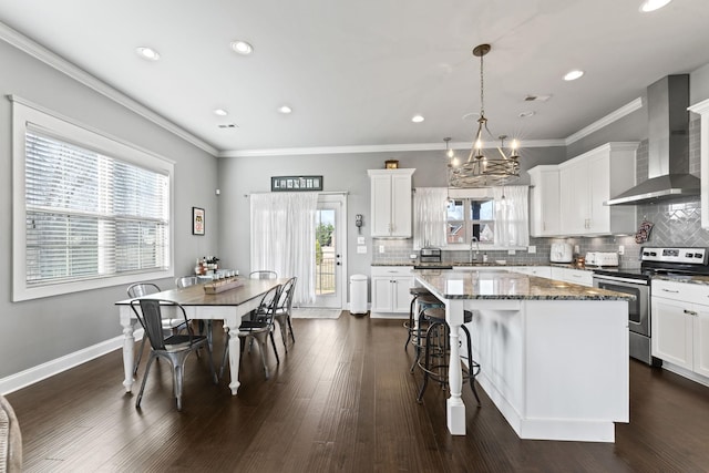 kitchen featuring a center island, hanging light fixtures, electric stove, dark stone counters, and wall chimney range hood