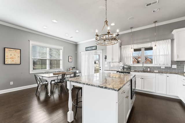 kitchen with light stone counters, crown molding, a center island, hanging light fixtures, and white cabinets