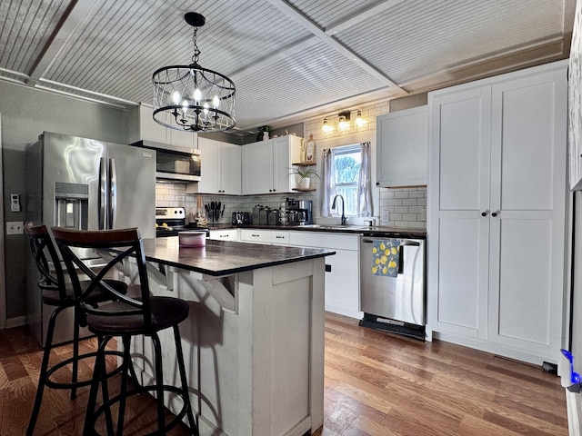 kitchen featuring decorative light fixtures, white cabinetry, hardwood / wood-style flooring, a center island, and stainless steel appliances