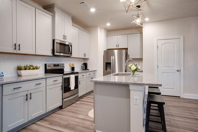 kitchen featuring white cabinetry, light stone counters, stainless steel appliances, and a center island with sink