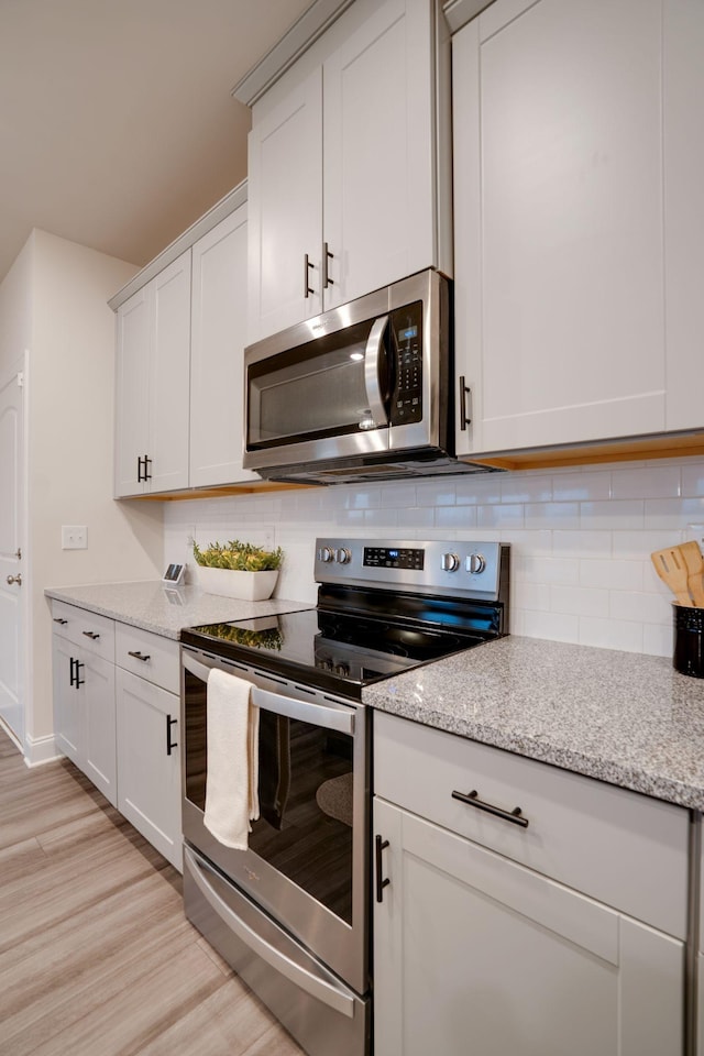 kitchen featuring white cabinetry, light stone countertops, decorative backsplash, and stainless steel appliances