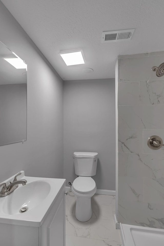 bathroom featuring tiled shower, vanity, toilet, and a textured ceiling