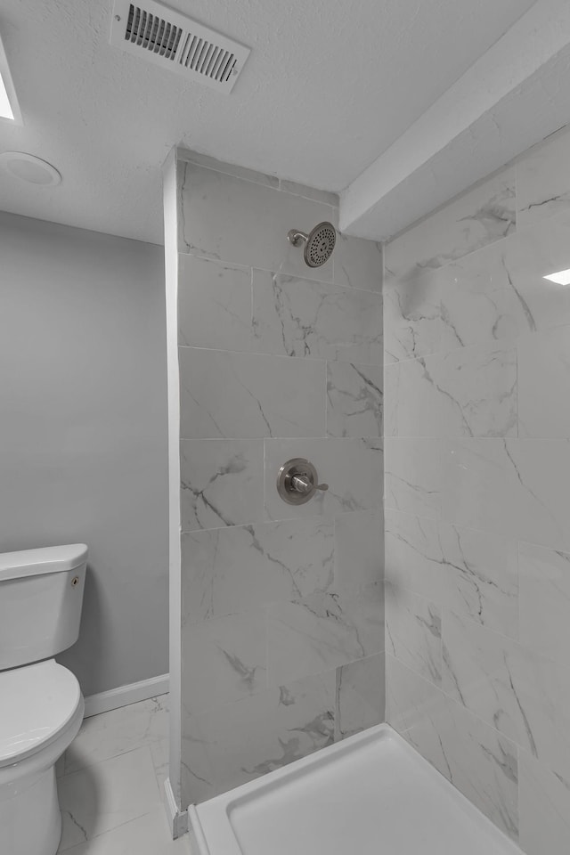 bathroom featuring a tile shower, a textured ceiling, and toilet