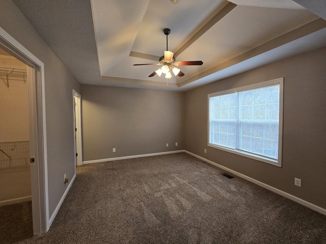 unfurnished bedroom with dark carpet, a tray ceiling, and ceiling fan