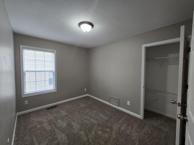 unfurnished bedroom with a walk in closet, a closet, a textured ceiling, and dark colored carpet