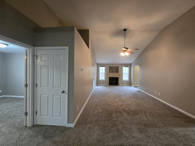 unfurnished living room with a tiled fireplace, vaulted ceiling, carpet floors, and ceiling fan