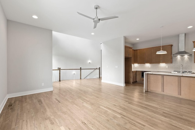 kitchen featuring pendant lighting, backsplash, light hardwood / wood-style flooring, and wall chimney exhaust hood