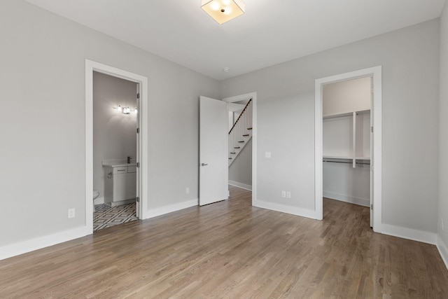 unfurnished bedroom featuring hardwood / wood-style flooring, ensuite bath, a spacious closet, and a closet