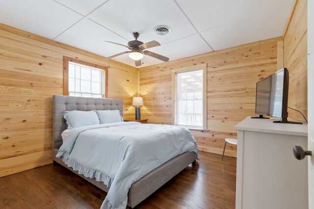 bedroom with ceiling fan, dark hardwood / wood-style floors, and wooden walls