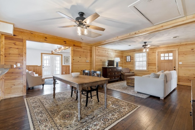 dining space with dark wood-type flooring, ceiling fan, and wood walls