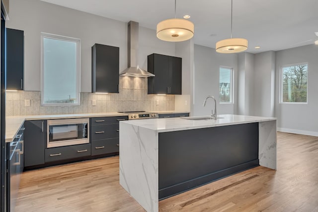 kitchen featuring a kitchen island, built in microwave, hanging light fixtures, light stone counters, and wall chimney exhaust hood