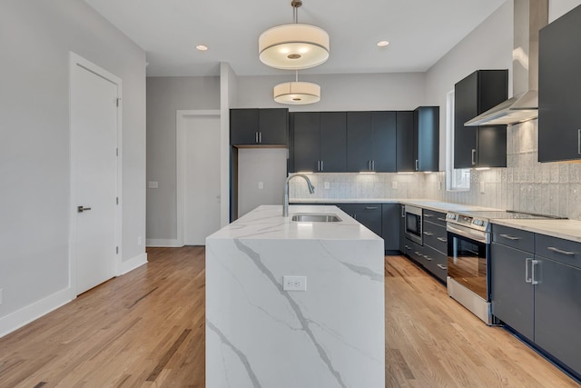 kitchen with stainless steel electric stove, decorative light fixtures, sink, a kitchen island with sink, and wall chimney range hood