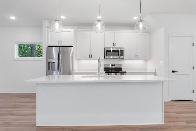 kitchen with sink, hanging light fixtures, appliances with stainless steel finishes, a kitchen island with sink, and white cabinets