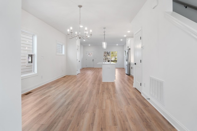 unfurnished living room featuring an inviting chandelier and light wood-type flooring