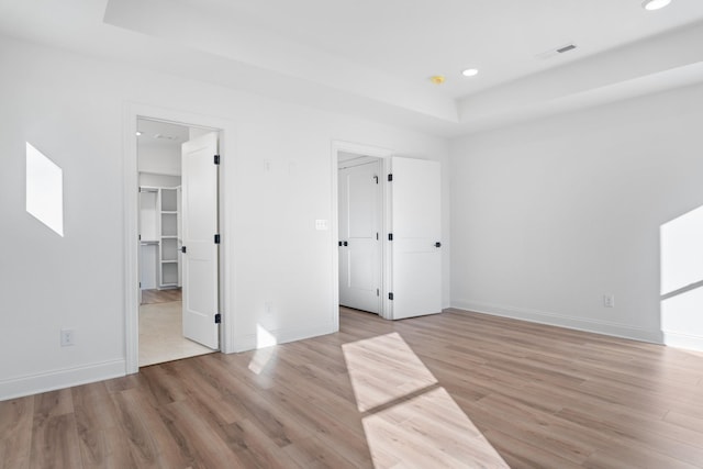 unfurnished bedroom featuring a spacious closet, light hardwood / wood-style floors, and a raised ceiling