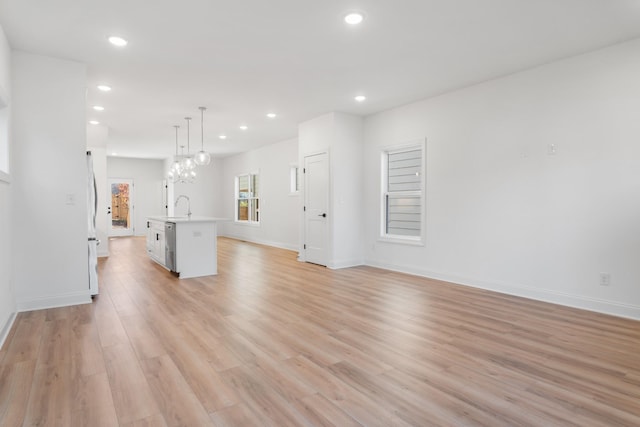 unfurnished living room with sink, a chandelier, and light hardwood / wood-style flooring