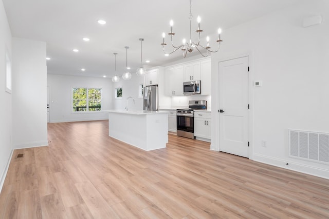 kitchen with decorative light fixtures, light hardwood / wood-style flooring, an island with sink, stainless steel appliances, and white cabinets