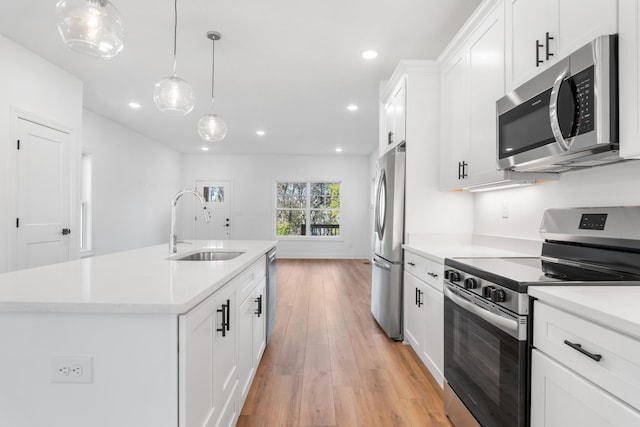 kitchen with sink, a center island with sink, appliances with stainless steel finishes, pendant lighting, and white cabinets