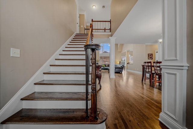 staircase with wood-type flooring, a high ceiling, and ornate columns