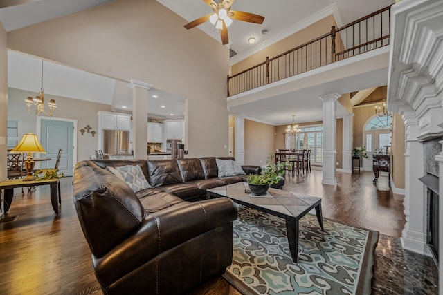 living room featuring ornate columns, crown molding, dark wood-type flooring, and ceiling fan with notable chandelier