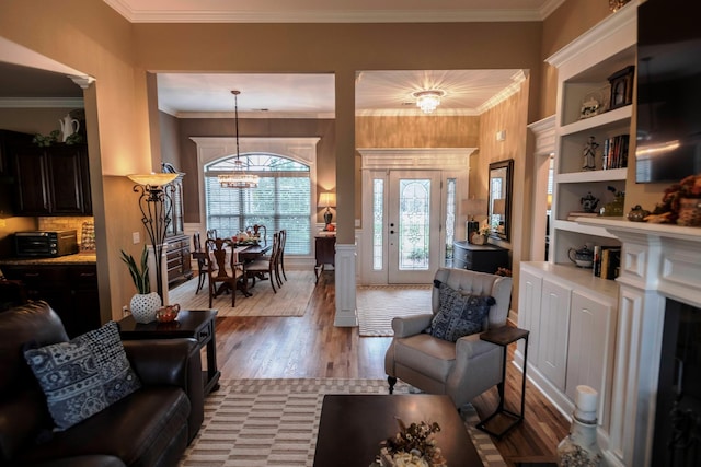 living room featuring a toaster, crown molding, an inviting chandelier, and wood finished floors