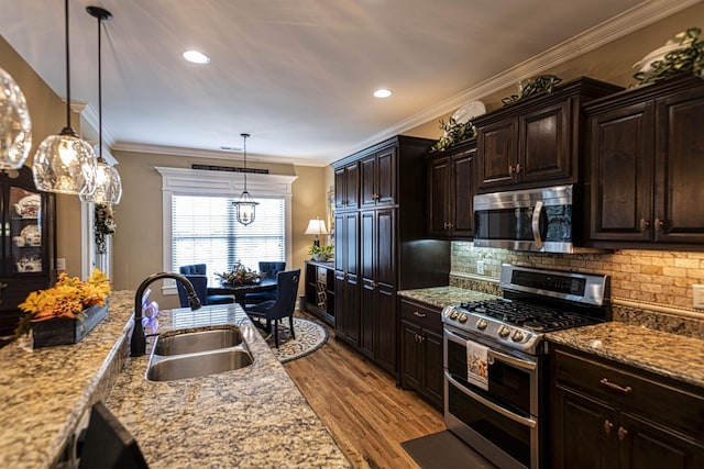 kitchen with dark brown cabinetry, sink, hanging light fixtures, stainless steel appliances, and light hardwood / wood-style floors