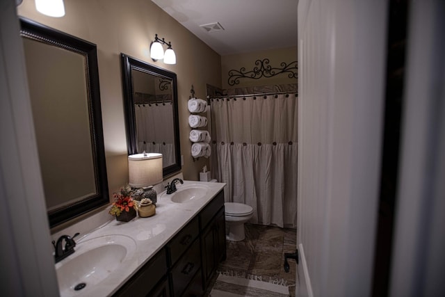 bathroom with toilet, double vanity, a sink, and visible vents