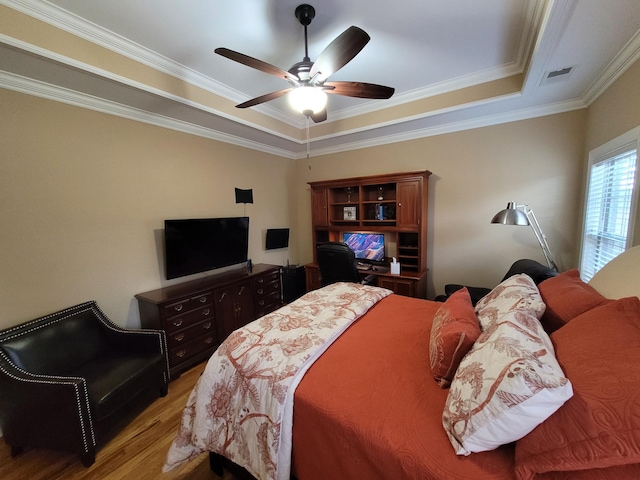 bedroom featuring visible vents, a raised ceiling, ceiling fan, ornamental molding, and wood finished floors