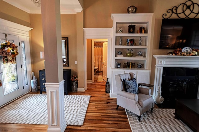 interior space with baseboards, wood finished floors, crown molding, ornate columns, and a fireplace