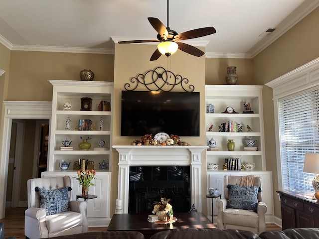 living room featuring built in features, visible vents, ceiling fan, crown molding, and a fireplace