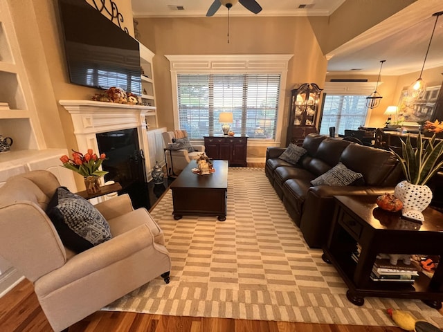 living area with built in features, ceiling fan, ornamental molding, light wood-style floors, and a fireplace