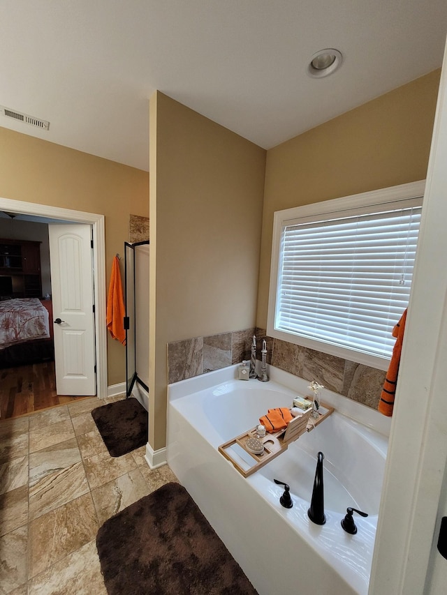 bathroom featuring visible vents, baseboards, a shower stall, a bath, and ensuite bath