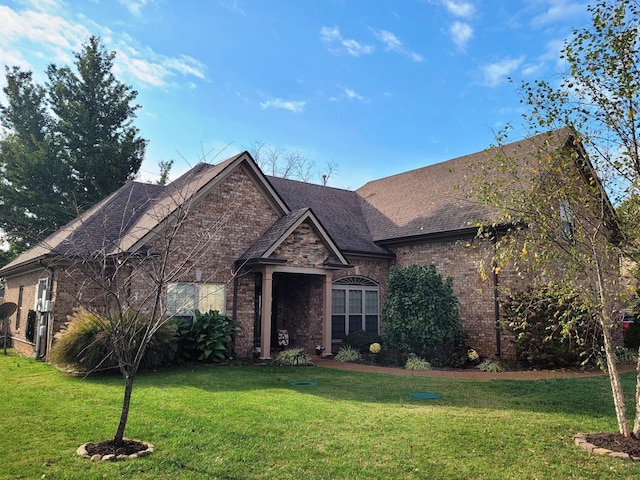 view of front of home featuring a shingled roof, a front yard, and brick siding