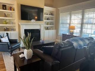 living area with plenty of natural light, built in shelves, wood finished floors, and a glass covered fireplace