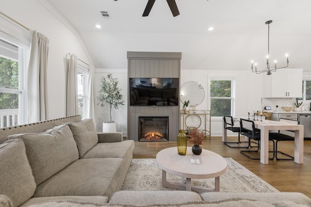 living room with ceiling fan with notable chandelier, a large fireplace, vaulted ceiling, and hardwood / wood-style floors