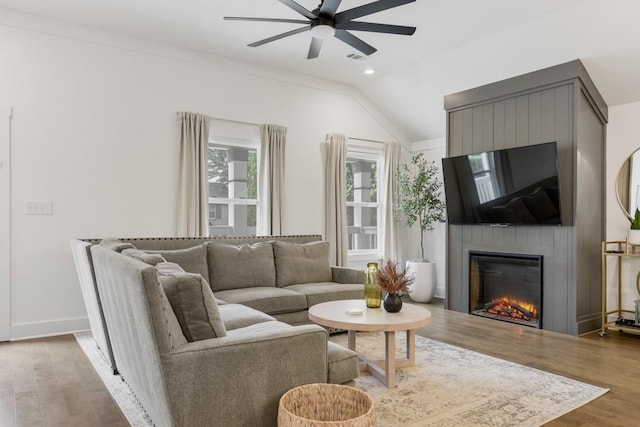 living room with hardwood / wood-style flooring, a large fireplace, ceiling fan, and vaulted ceiling