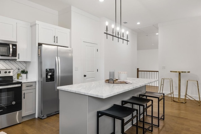 kitchen with a kitchen island, appliances with stainless steel finishes, white cabinetry, hanging light fixtures, and light stone countertops