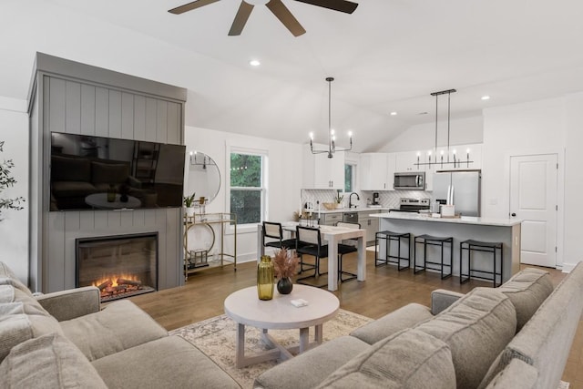 living room with a large fireplace, sink, vaulted ceiling, and hardwood / wood-style floors