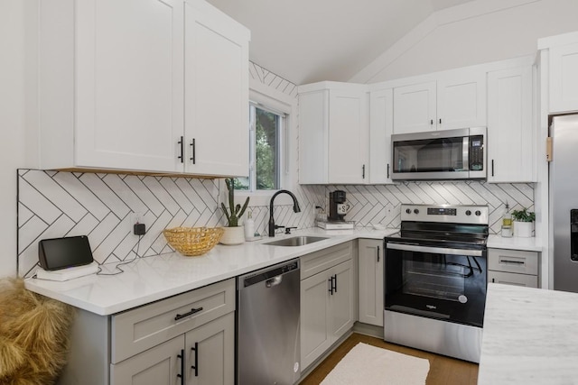 kitchen with appliances with stainless steel finishes, tasteful backsplash, lofted ceiling, sink, and white cabinets