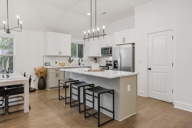 kitchen with stainless steel appliances, a kitchen island, white cabinets, and decorative light fixtures