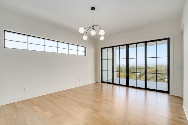 empty room featuring an inviting chandelier, light hardwood / wood-style flooring, and a wealth of natural light