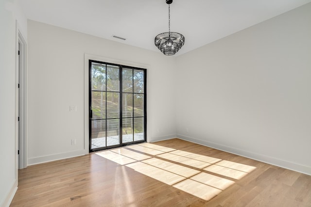 empty room featuring an inviting chandelier and light hardwood / wood-style flooring