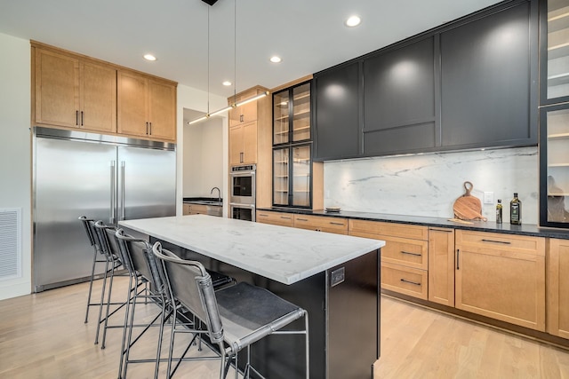 kitchen featuring a breakfast bar area, dark stone countertops, an island with sink, pendant lighting, and stainless steel appliances