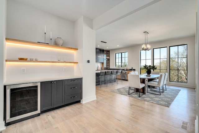 interior space featuring a chandelier, beverage cooler, light hardwood / wood-style floors, and decorative light fixtures