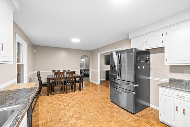 kitchen with dark stone countertops, stainless steel fridge, light parquet floors, and white cabinets