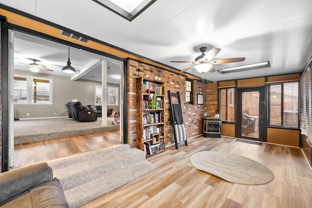 living area featuring a skylight, light hardwood / wood-style floors, ceiling fan, and brick wall