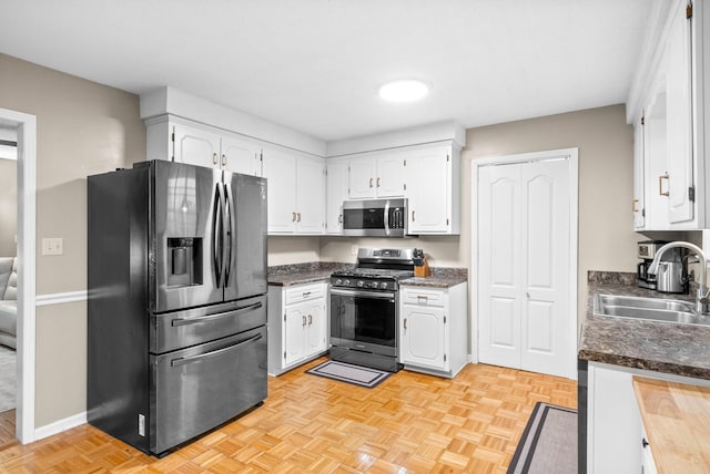 kitchen featuring light parquet flooring, stainless steel appliances, sink, and white cabinets